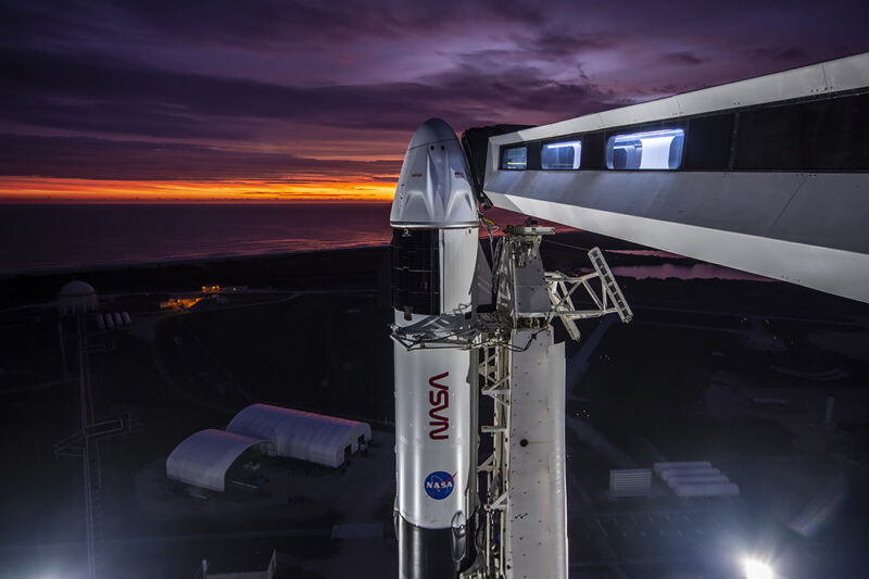 A rocket sits on a launch pad under a purple and gold streaked dawn.